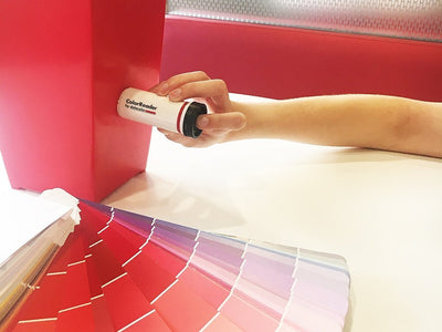 A person using the Datacolor Color Reader on a red object to determine the closest paint color match, available at John Boyle Decorating Centers in Connecticut.